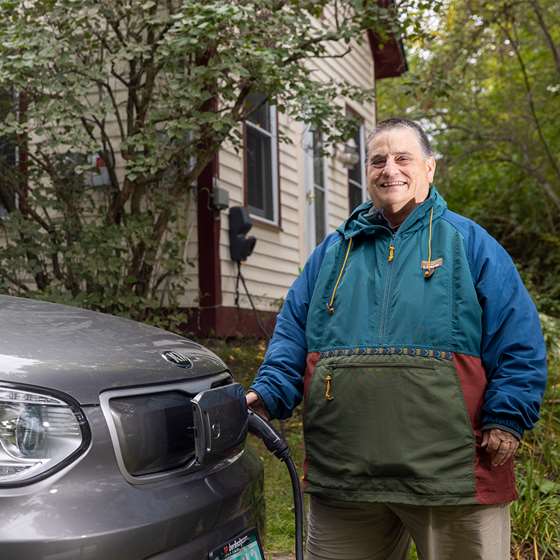 older man standing next to an electric car that is plugged into a charger