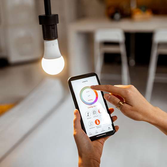 hands holding a smartphone near an LED bulb that shows an app