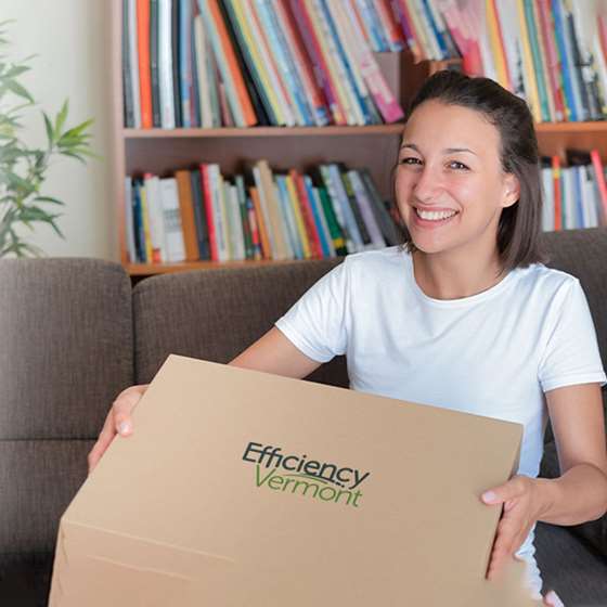 a smiling young white woman holding a box with Efficiency Vermont logo
