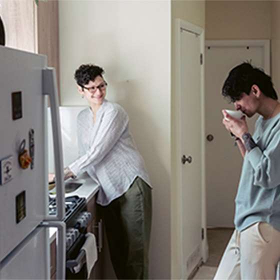 two adults talking in a small kitchen with a refrigerator in the foreground