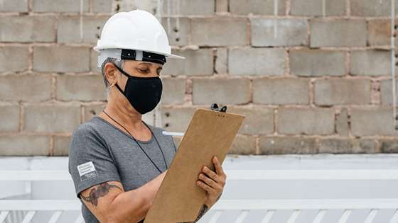 A contractor wearing a mask writes something down on her clipboard