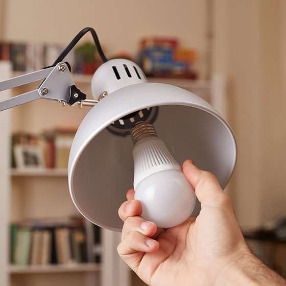 A hand changes a lightbulb in a desk lamp