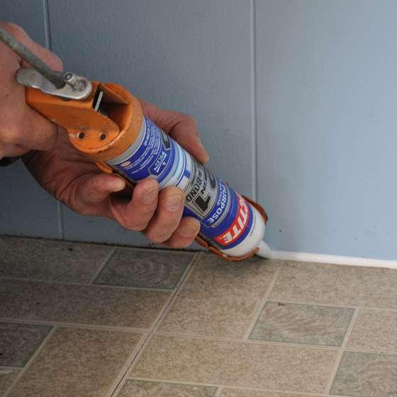 Someone caulks the bottom of a wall