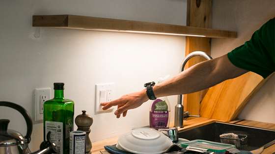 white person reaching for a light switch over a kitchen sink