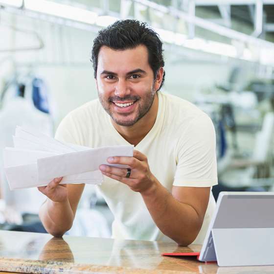 A smiling man holds papers at the front desk of a small business