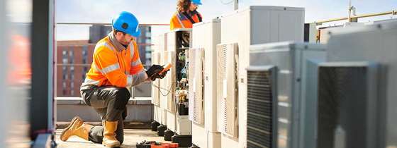 HVAC technicians in hard hats and orange reflective gear and boots servicing rooftop HVAC system