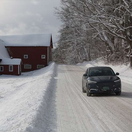 an EV driving on a snowy road near red barn