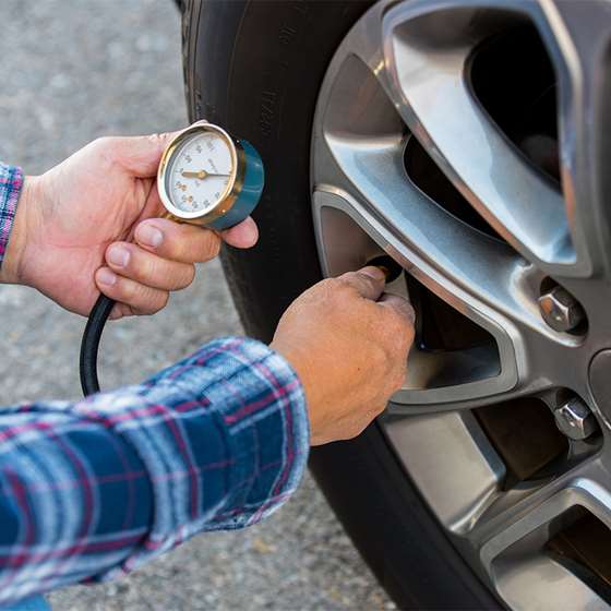 wgite man in flannel shirt holding tire pressure gauge in front of car tire