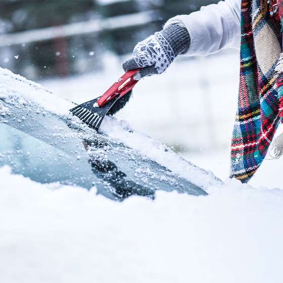 person scraping snow and ice off from a car windshield