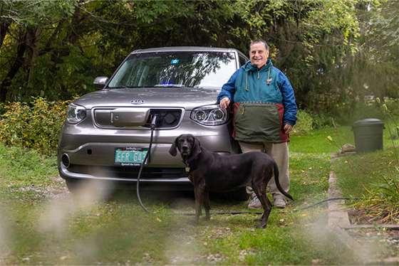 man charging an electric car in a gravel driveway with his dog 