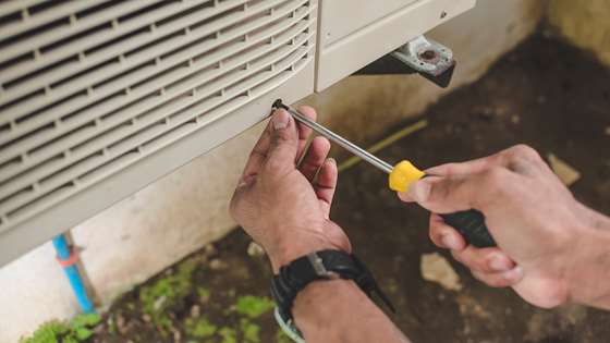 outdoor heat pump compressor with a screwdriver opening the unit for maintenance
