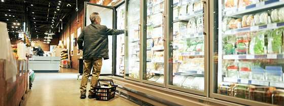 A white man reaches his arm into an open refrigerator at a grocery store