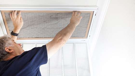 A man changes the filter in a ceiling vent