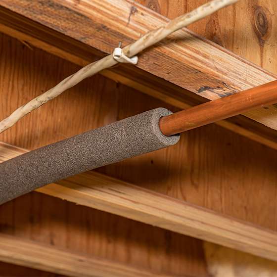 a copper pipe in a floor joist with gray foam insulation sleeve