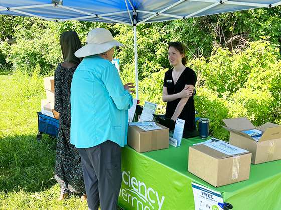 Efficiency Vermont staff person behind an event table talking with a younger woman wearing a head scarf and an older woman wearing a sun hat