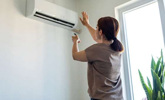 woman in front of a heat pump wall unit with remote control