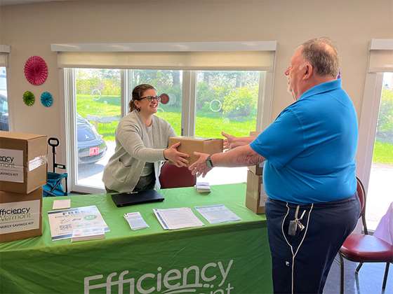 Efficiency Vermont staff person handing an box to an older man at an event table