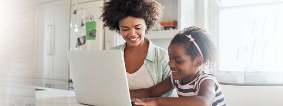A black woman sits in front of a computer with a black girl