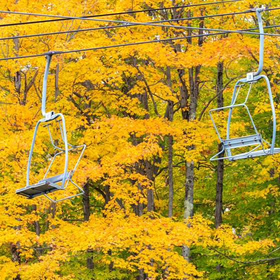 Two empty chair lifts in front of beautiful yellow foliages