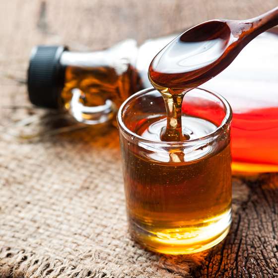 A spoon drizzles maple syrup into a small glass on a table