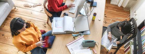 view looking down at a modern dining room table with family on computers and tablets, working and doing homework