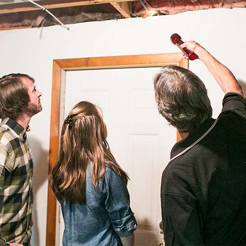 A contractor talks with a homeowner while examining exposed insulation in a basement ceiling