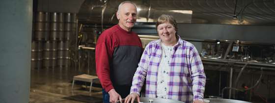 A couple stands behind a barrel of maple syrup