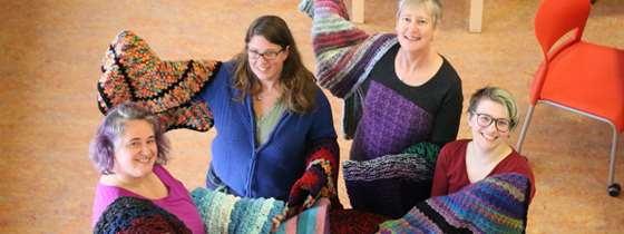 Image of several Efficiency Vermont employees holding blankets they knitted to give to customers.