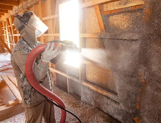 a person with PPE installing insulation with a hose and blwn in materials