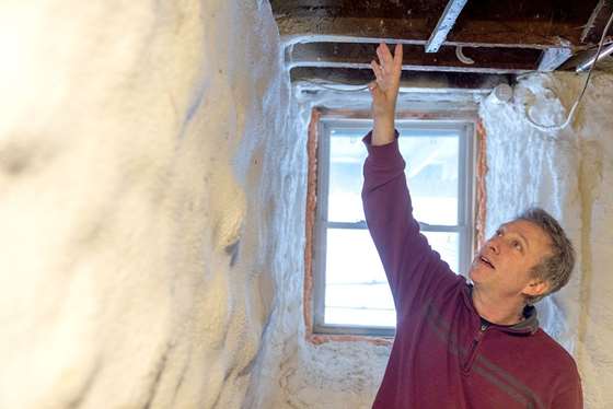 man inspecting spray foam insulation between basement ceiling joists