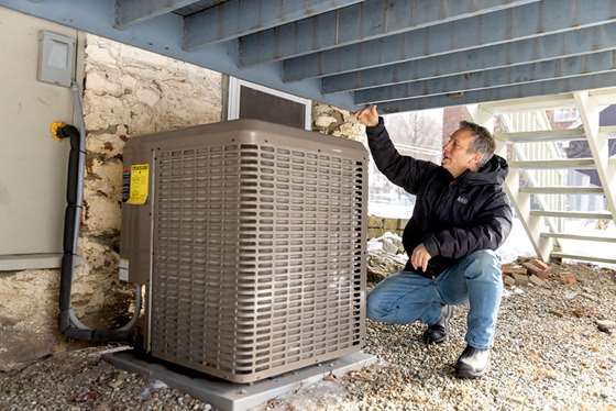man showing the heat pump outdoor condenser unit  installed under a wooden deck 