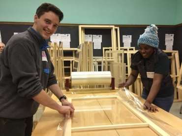photo of a young white man and a young black woman working on a wooden window frame in a workshop environment
