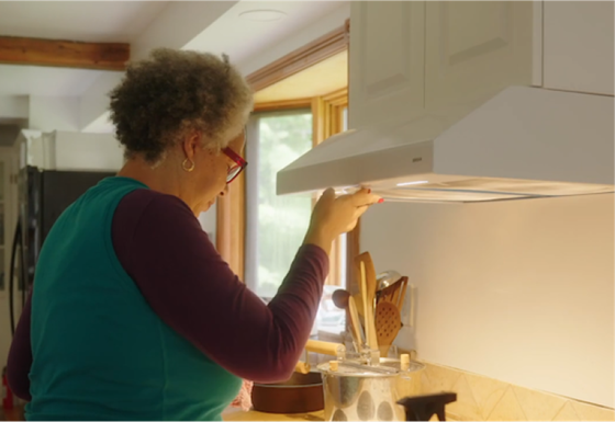 a woman of color wearing glasses stands in front of her kitchen stove demonstrating challenges to the kitchen range hood in front of her