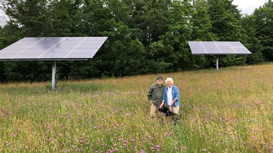 Richard Carr and his wife stand in the field outside their house in front of their first solar panels