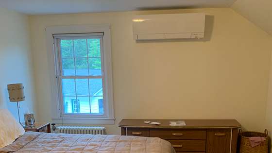A bedroom with a ductless heat pump on the wall