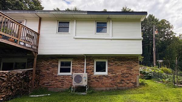 exterior of a raised ranch style home with brick and white siding, a heat pump outdoor compressor is sitting on a platform near the house