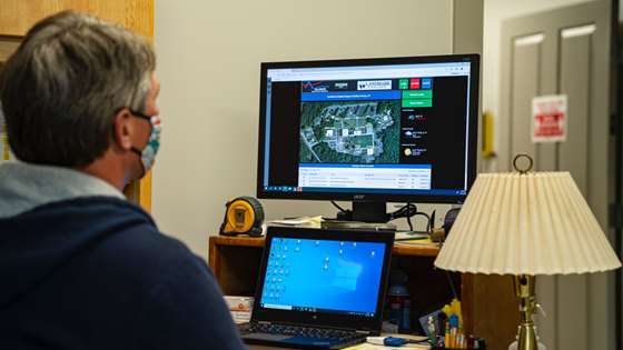Kyle Skrocki, wearing a mask, sits at his computer demonstrating the controls