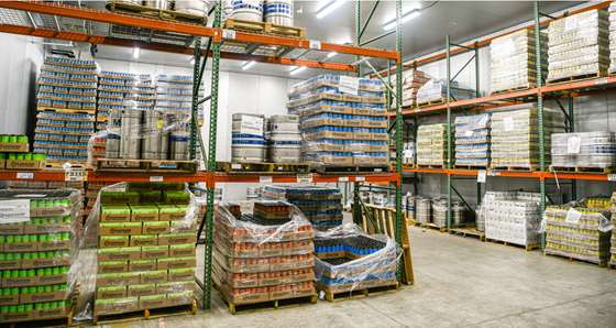 large cooler with warehhouse shelves full of pallets with canned beer and some kegs