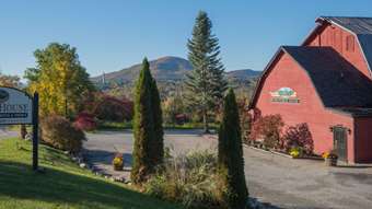 Photo of Publyk  House, which is a large, red barn-looking building set on a sunny country road with the leaves just starting to change. A sign that says Publyk House is to the left of the building. Hills are in the distance beyond the Publyk House.