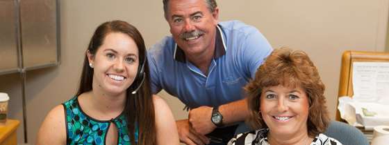 Three people smile at the camera in an office