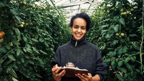 A woman of color standing with some produce talks to a white woman with a clipboard